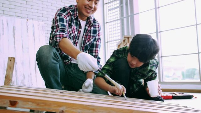 Young male carpenter teaching his son how to work with wood in workshop.