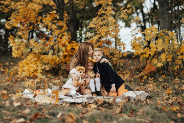 Young family sitting on a picnic blanket, embracing and enjoying a beautiful autumn picnic in nature. Happy family having picnic in park.