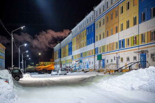 Snowy street of the northern city. Winter night cityscape. Cars and snowdrifts near multi-colored panel buildings. Winter in the Arctic. The city of Anadyr, Chukotka, Siberia, Far East of Russia.