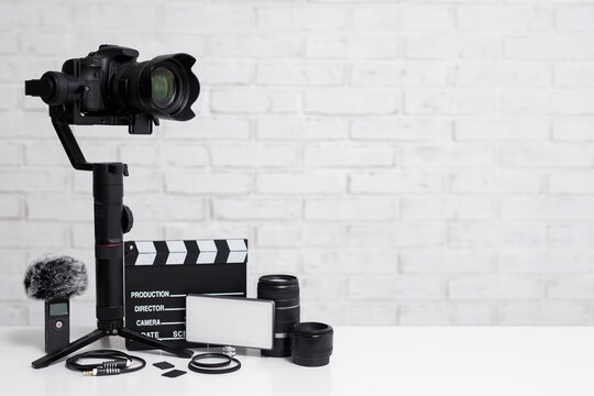 videography concept - modern dslr camera on 3-axis gimbal stabilizer, lenses, microphone, led light, clapper board and other videography equipment over white brick wall background