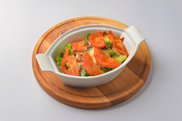 Baked mixed vegetable casserole with broccoli and tomatoes. Served in a white pot over white background.