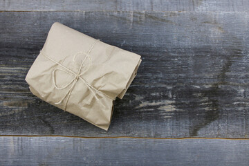 Gifts goods wrapped in craft paper and tied with a scourge on rough woodboard background. Eco-friendly packaging. Zero waste. Copy space
