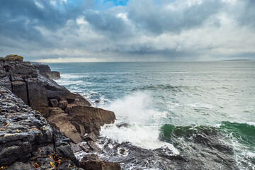 Powerful waves hit the rough stone coast line creating huge splashes of water. Low dark storm clouds, West of Ireland. Nobody.