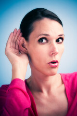 Studio photo of dark woman holding up hand to ear, eavesdropping, listening.