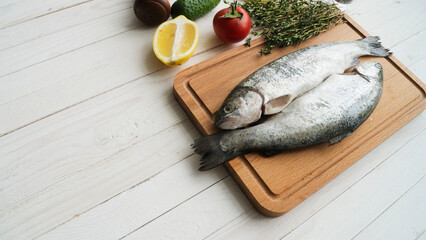 Two rainbow trout on a board, with herbs , ready for cooking.