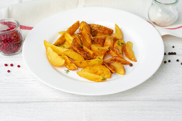 Fried potato wedges in plate on white wooden table