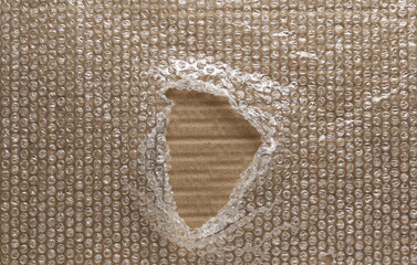 Blank cardboard covered with torn bubble wrap that has hole in middle background and texture