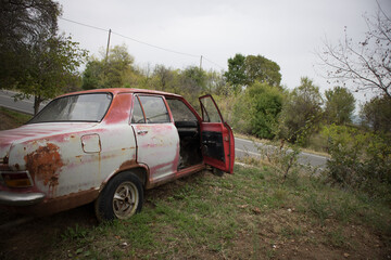 An abandoned antique car, with faded red color. The front passenger door is open.
