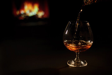 Pour brandy into a glass against the background of the fireplace