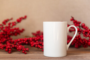 Obraz na płótnie Canvas Mockup - White cup on Christmas holly berry background. Coffee or tea mug