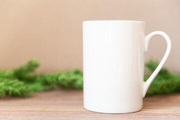 White cup on Christmas tree branches background. Cofee or tea mug for your design, mockup