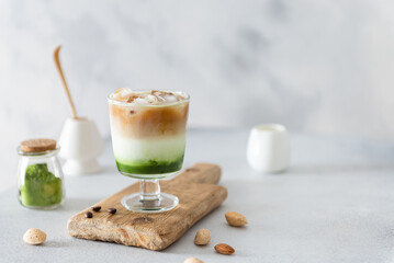 Matcha green tea latte in a glass on wooden board. Iced matcha espresso. Trendy layer spirulina drink with ice. Side view, copy space. Menu, recipe. Coffee shop