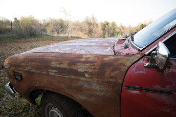 View from the left side, of an old car with faded red colour.