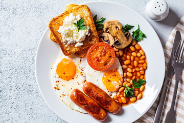 English breakfast with sausages, beans, fried eggs, toast, mushrooms and tomatoes in white plate. English breakfast concept.