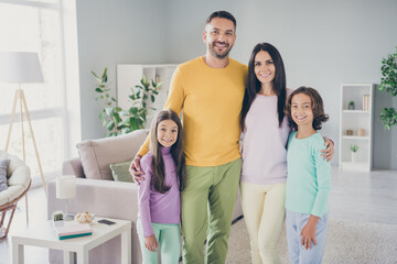 Photo of full family four members meeting two small children cuddle look camera wear colorful pullover pants in living room indoors