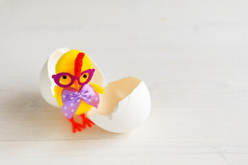 One chick with an egg shell. Toy yellow chicken with glasses and a bow