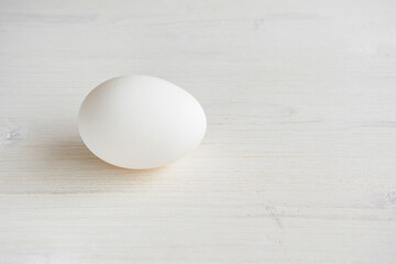 Single white egg on a white wooden background