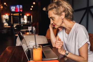 Smiling senior female blogger in casual wear sitting in coffee shop using laptop