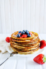 Close-up delicious pancakes, with fresh blueberries, strawberries and maple syrup on a light background. With copy space. Pile of small homemade pancakes with forest fruits.