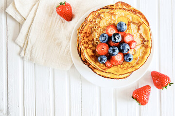 A stack of pancakes decorated with berries. delicious pancakes, with fresh blueberries, strawberries and maple syrup on a light background. With copy space. Top view.