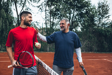 middle aged father with his son on tennis court