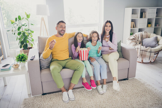 Photo of big full family four members sit sofa eat pop corn watch comedy series laugh wear colorful jumper trousers in living room indoors
