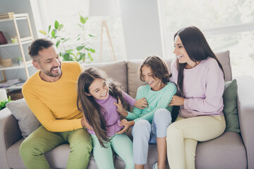 Photo of full big family four members sit couch enjoy tickling wear colorful sweater trousers in living room indoors