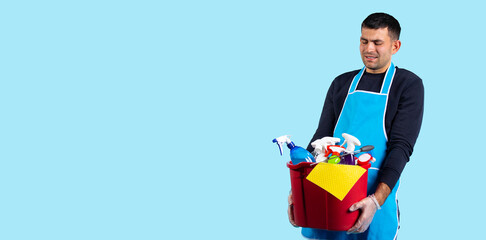 Banner, long format. A man is holding a heavy bucket with various cleaning products. Gender equality. Photo on blue background with empty side space