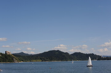 Blue waters of Czorsztyn dam lake with yacht and green hills and mountains and blue sky with clouds in summer in southern Poland