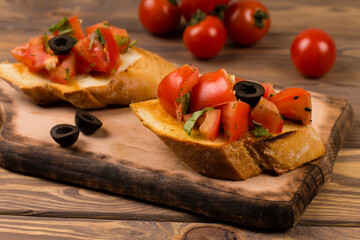 Bruschetta with tomatoes, olives, mozzarella and basil on a wooden background. Traditional Italian snack or appetizer, antipasto.