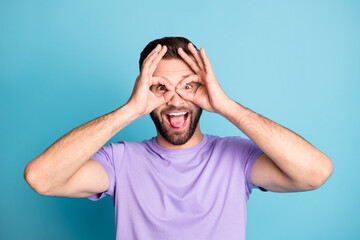 Photo of young excited crazy man tongue-out happy smile have fun binoculars eyes isolated over blue color background