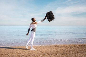 Portrait of a young black boy picking up a suitcase on the beach. Concept of travel.