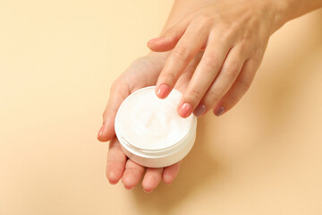 Cute female hands hold jar of cosmetic cream on beige background