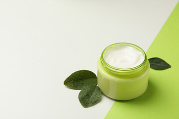 Jar of cosmetic cream and leaves on two tone background