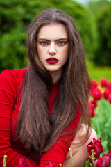 Young beautiful brunette model posing on a background of red tulips