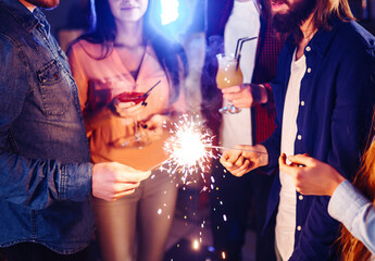 Christmas sparkles in hands. A crowd of young happy people with sparklers in their hands during celebration. Sparkling lights of bengal fires 2021.