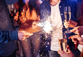 Christmas sparkles in hands. A crowd of young happy people with sparklers in their hands during celebration. Sparkling lights of bengal fires 2021.