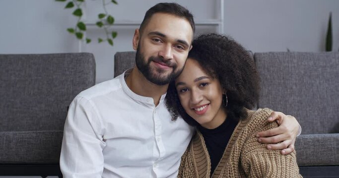 Portrait of multi-ethnic couple Caucasian man and African American woman young girl newlyweds girlfriend and boyfriend hugging sitting on sofa cuddling each other looking at camera and smiling closeup