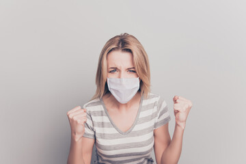 Close up portrait of furious woman showing fists wearing white face mask isolated on gray background