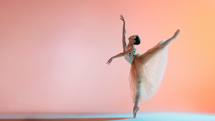 Young slim ballerina in light long dress is dancing on colored background with backlight - obrazy, fototapety, plakaty