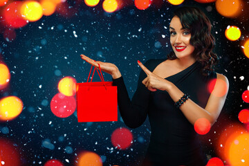 Black friday sale concept for shop. Shopping girl holding red bag isolated on dark background at shopping on blackfriday. Woman pointing to looking left on copy space.