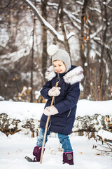 Girl child walking in the winter forest in a blue jacket and gray hat, snow and snowflakes, frosty air, baby's smile