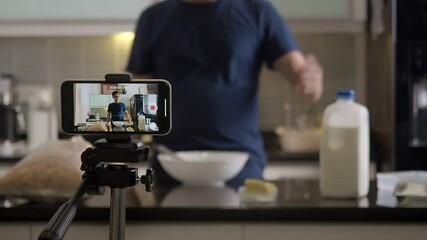 Young asian man blogger and vlogger and online influencer live streaming a bakery cooking show on social media using a smartphone at home kitchen.