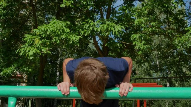 TeenA cute boy 12-15 years old in a blue T-shirt is pushing up from an iron bar. The schoolboy goes in for sports on the street. High quality 4k footage