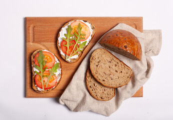 Whole grain bread sandwiches with ricotta cheese, tomato, arugula. On a wooden board. White background.