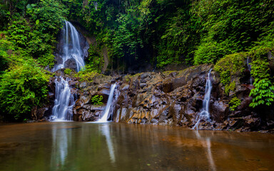 Waterfall landscape. Beautiful hidden Pengibul waterfall in rainforest. Tropical scenery. Water reflection. Slow shutter speed, motion photography. Nature background. Bali, Indonesia