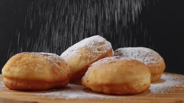 many fresh baked doughnuts or berliners rotating on a wooden cutting board close-up. pouring many powdered sugar