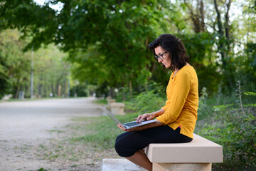 Obraz premium portrait of beautiful and cheerful mature woman working outdoor in a park with wireless connection and a laptop computer