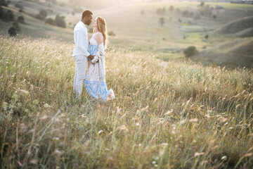 Fototapeta na wymiar Stylish diverse pregnant couple on the meadow in embrace