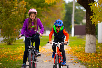 Children in helmets ride bicycles in the park. Outdoor recreation. Autumn Park. Photo with empty side space